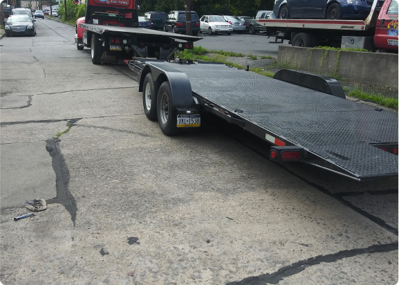 A red flatbed tow truck sits with a second flatbed hooked behind it. Both beds are empty