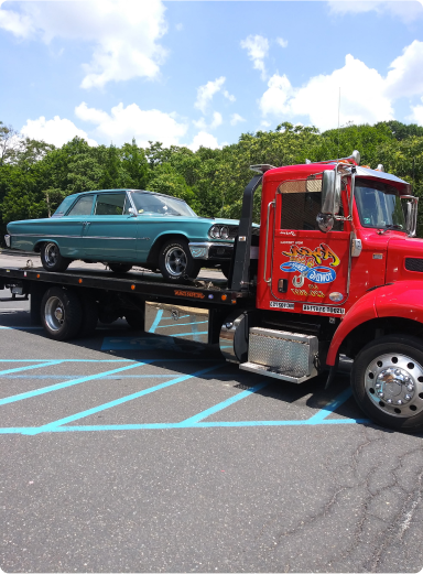 A classic teal muscle car on the flatbed of a red Azar tow truck in a parking lot.