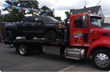 A black pickup truck sits on the flatbed of an Azar tow truck.