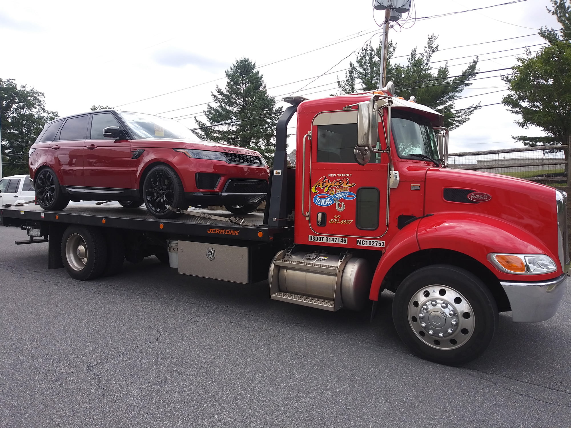 A red-cabbed Azar flatbed tow truck hauling a red luxury SUV out of a parking lot
