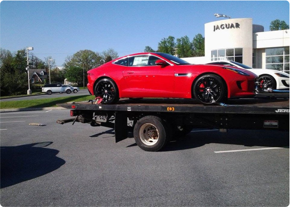 A luxury red car parked on the back of a flatbed transport tow truck at a Jaguar Dealership