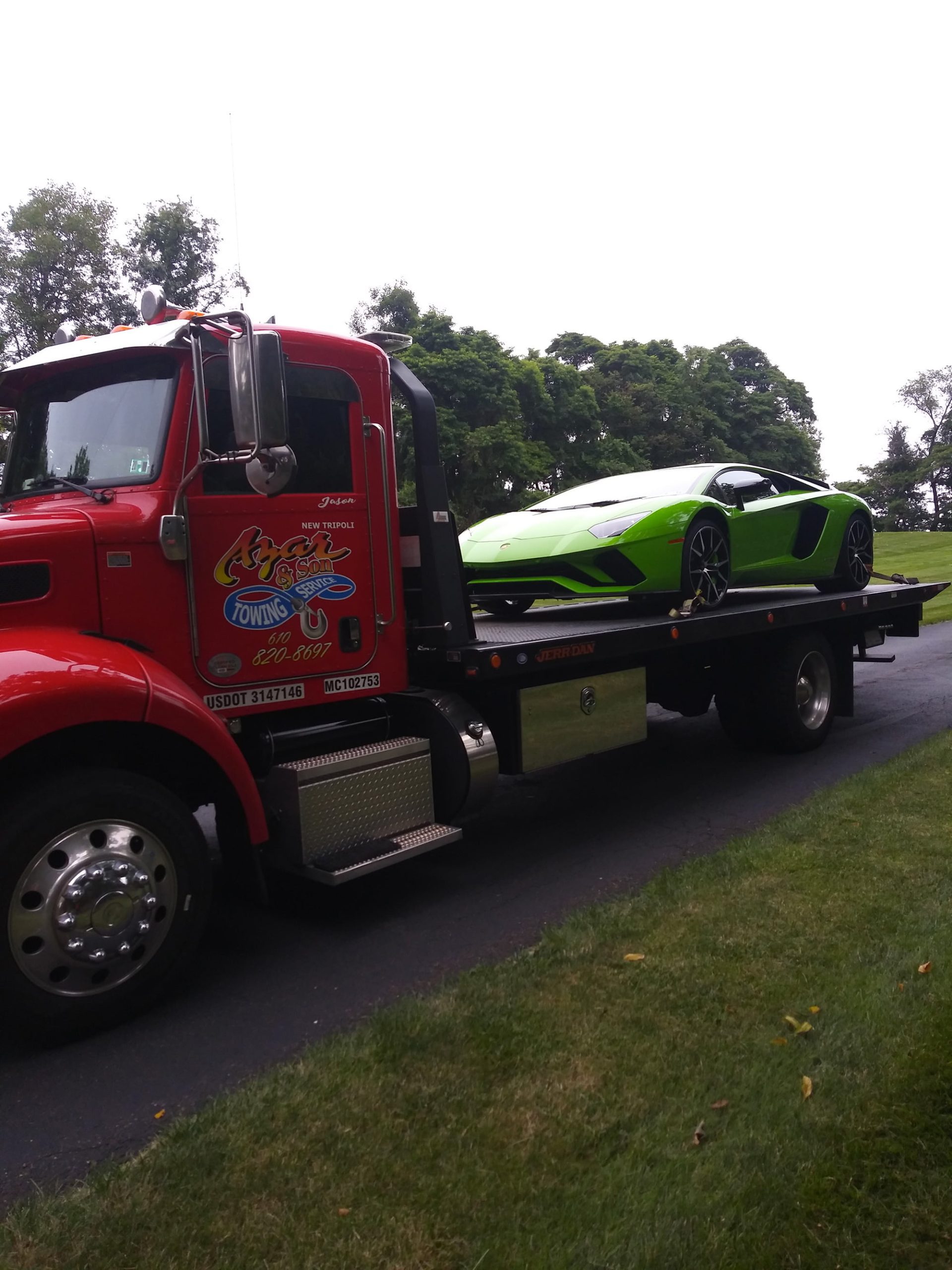 A green sports car sits on a red-cabbed Azar tow truck