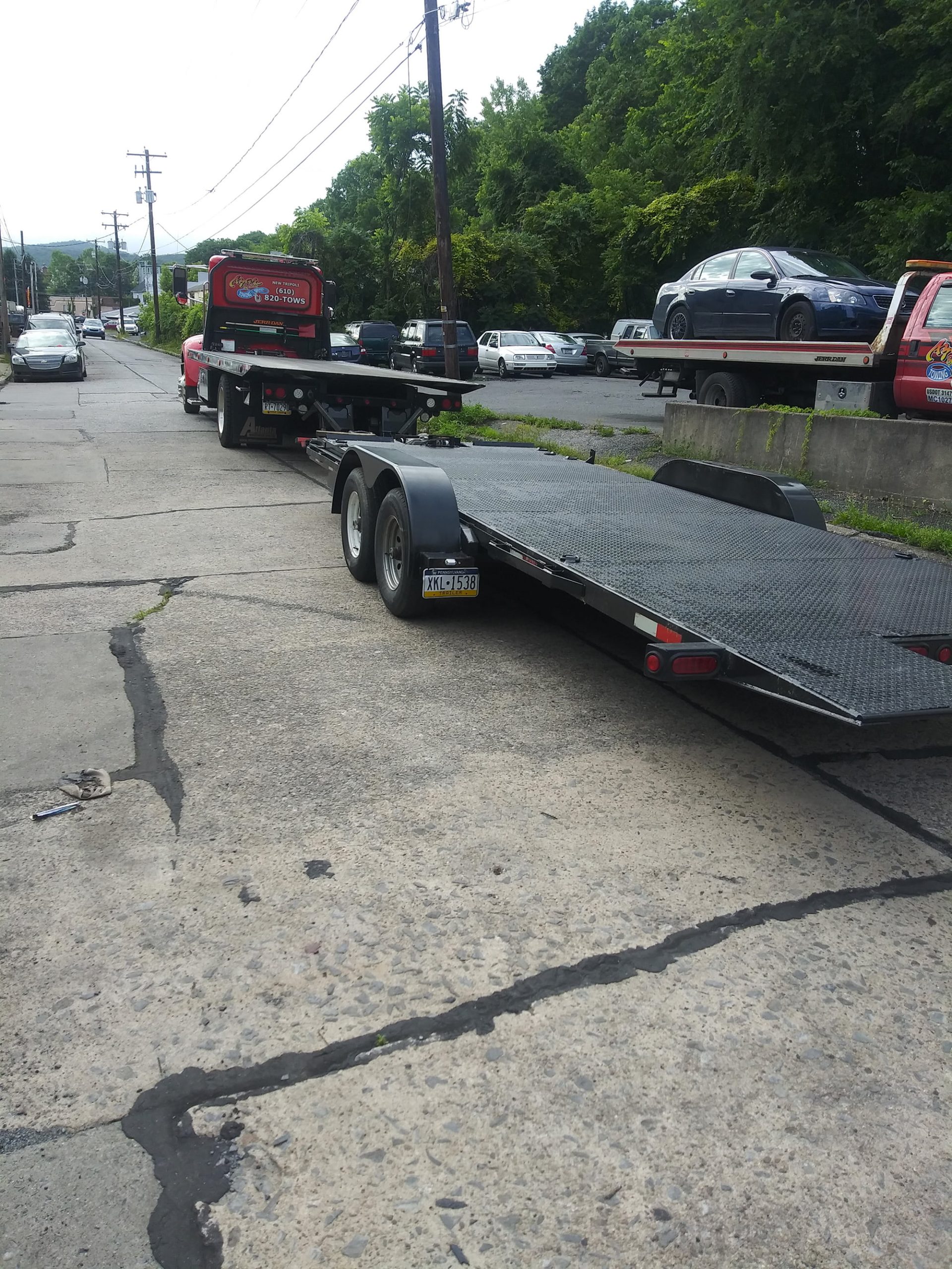 A red flatbed tow truck sits with a second flatbed hooked behind it. Both beds are empty.