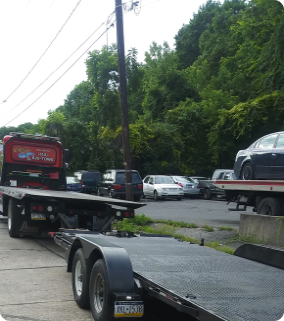 A red flatbed tow truck sits with a second flatbed hooked behind it. Both beds are empty.