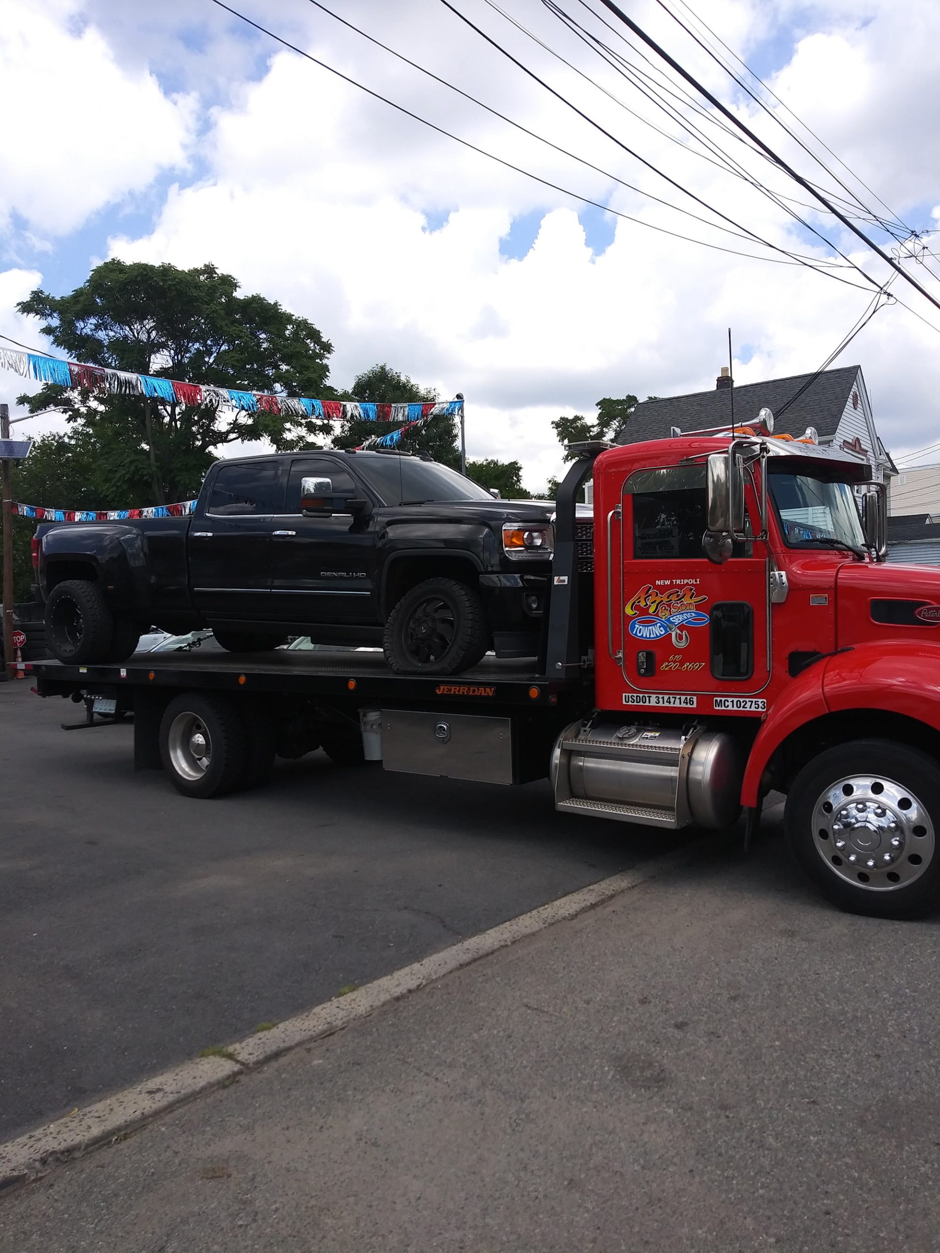 A black pickup truck sits on the flatbed of an Azar tow truck