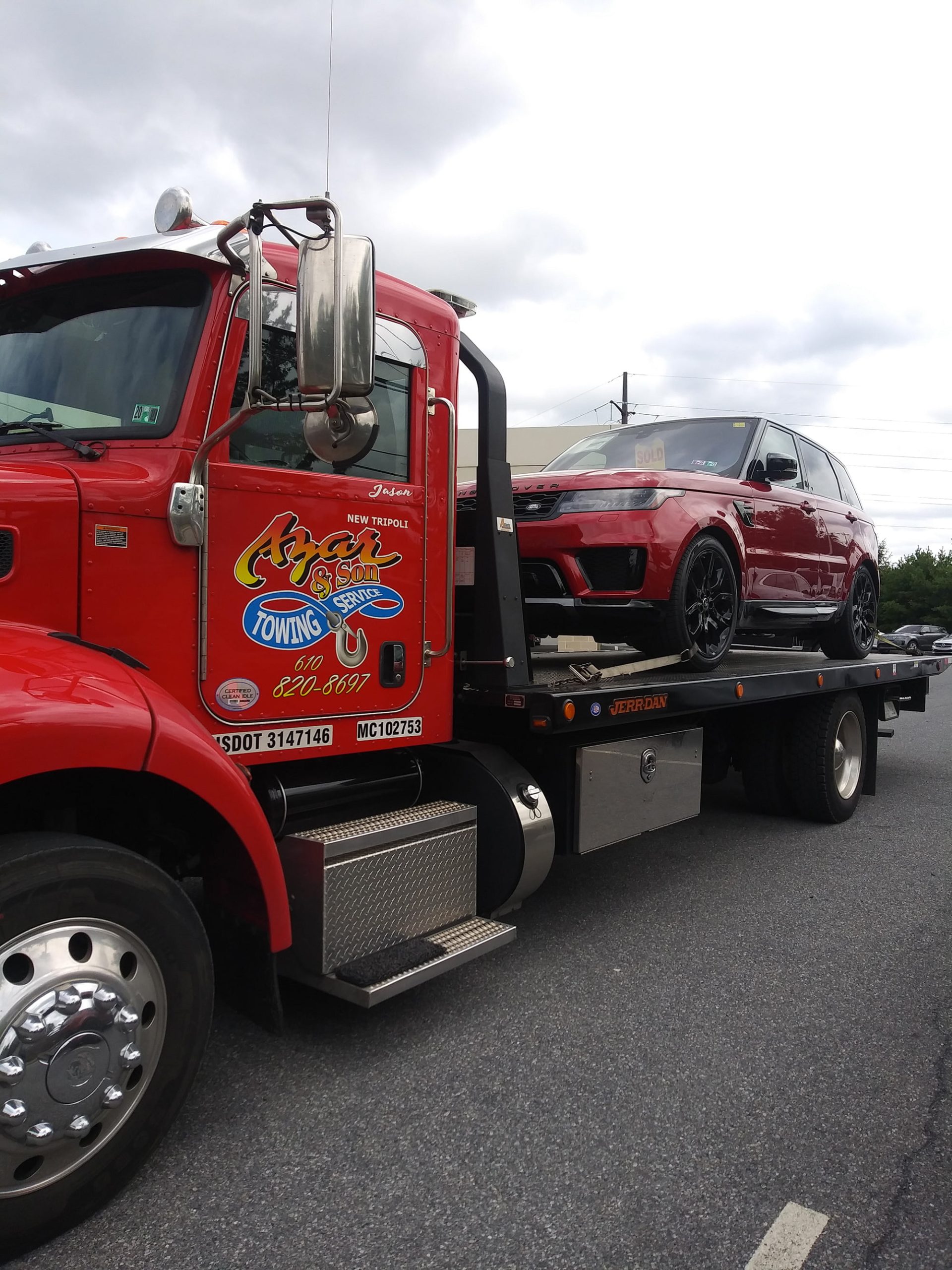 A red-cabbed Azar flatbed tow truck hauling a red luxury SUV