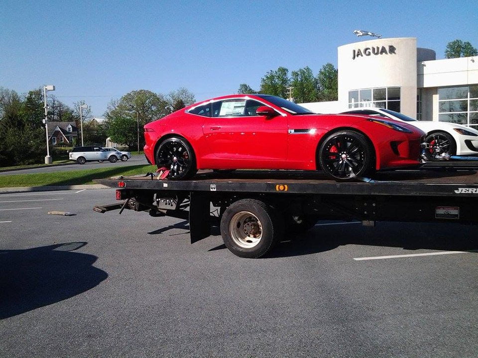 A luxury red car parked on the back of a flatbed transport tow truck at a Jaguar Dealership