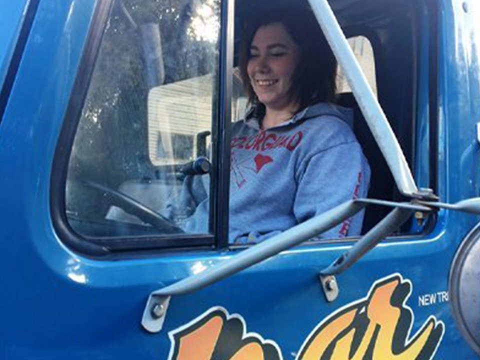A young woman smiles in the driver's seat of an Azar tow truck.